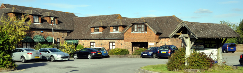 Two-storey brick buildings on two sides of a car park, with a covered sign in the foreground