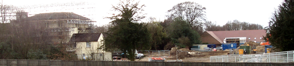 To the left, a large white building surrounded by scaffolding, and to its right a new brick building